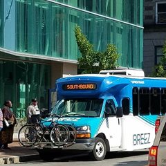 A public transport bus at a bus stop picking up passengers with bikes in the bike rack on the front.