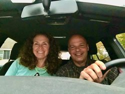 A man and a woman in a car smiling.