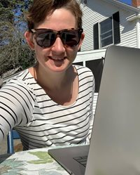 A woman working on her laptop outside her house.