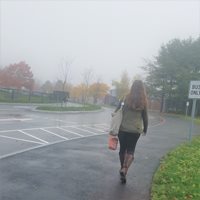 A woman walking to work on a sidewalk on a misty day.