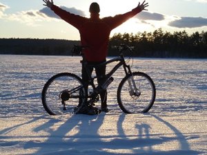 A man posing next to his bike in the snow.